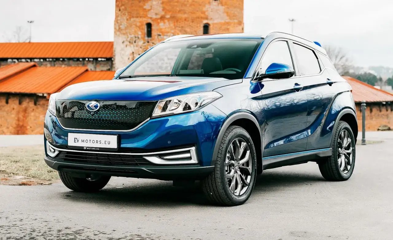 Błękitny SUV EV z nowoczesnym grillem, zaparkowany przed ceglanymi budynkami. Jego lśniąca karoseria odbija otoczenie, a felgi dodają mu sportowego charakteru. Idealny do miejskich podróży i odkrywania nowych miejsc.