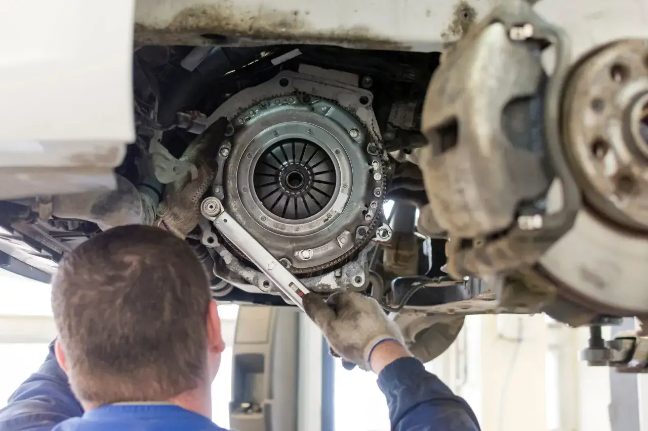 Mechanik pracuje przy skrzyni biegów, wymiana sprzęgła kosztuje, gdy auto wymaga naprawy.