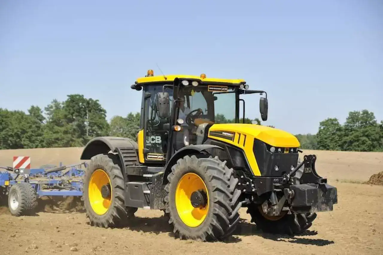 Żółty traktor JCB Fastrac z przyczepionym pługiem pracuje na polu w słoneczny dzień.