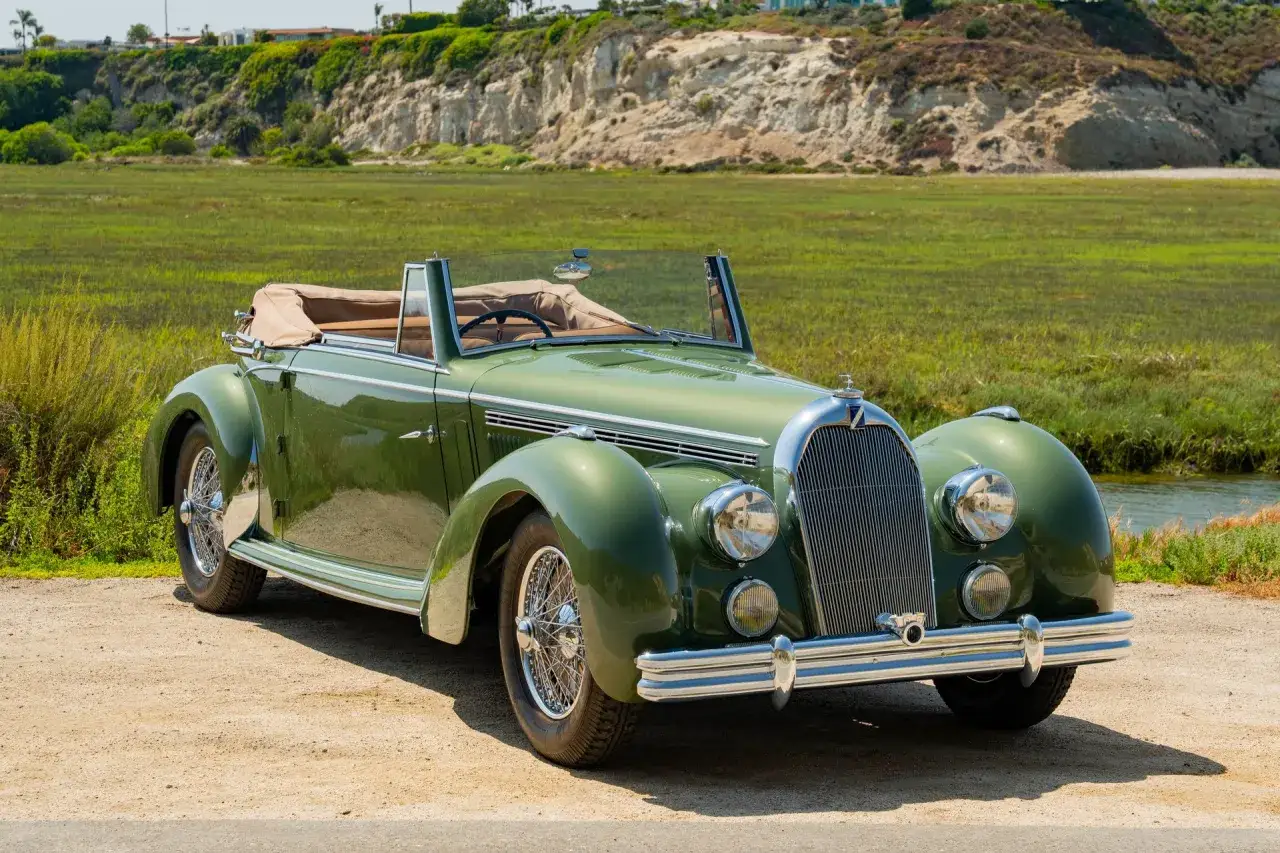 Zielony kabriolet Talbot z lat 30. XX wieku, z chromowanymi detalami, zaparkowany na piaszczystej drodze przy malowniczej, trawiastej równinie.